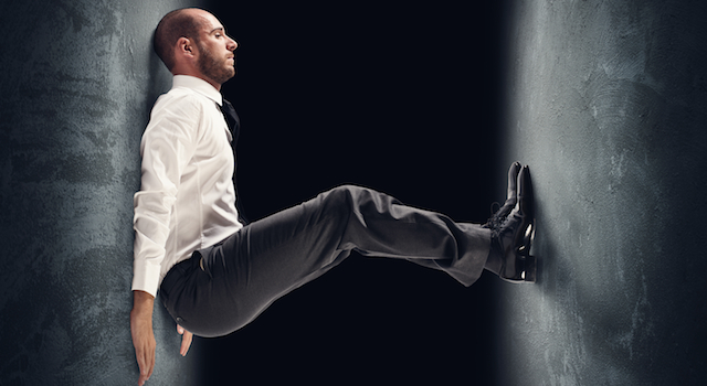 A man in business clothes pushes back against two concrete walls